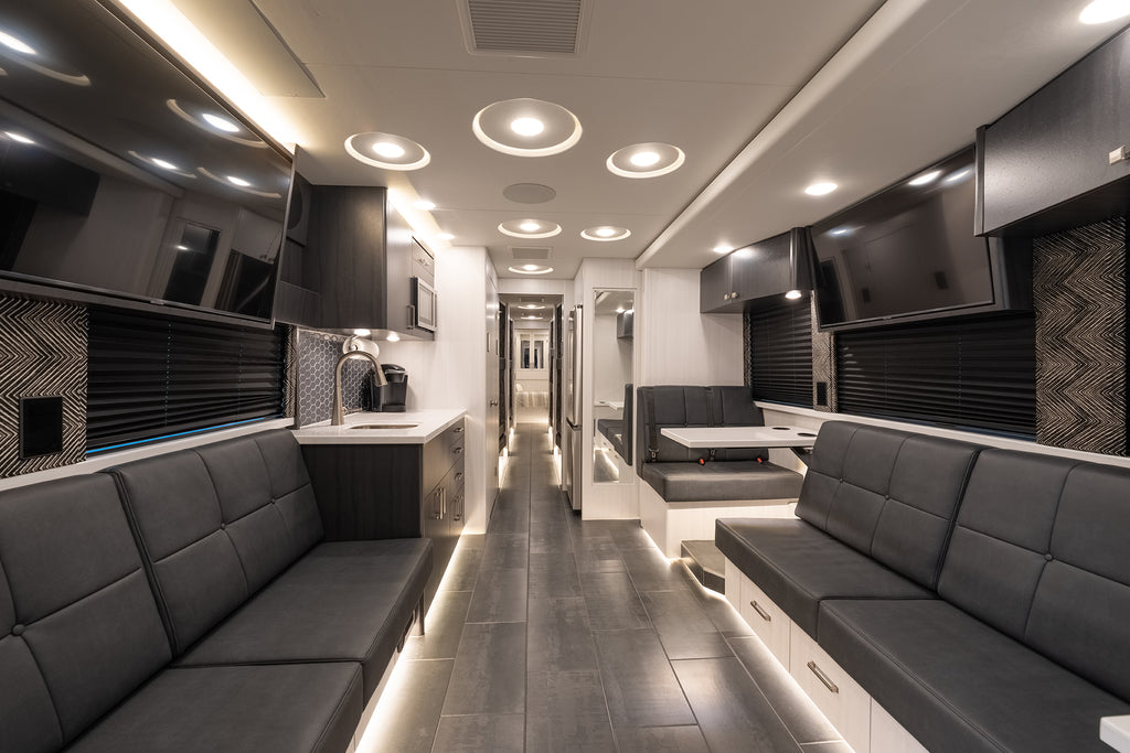 Modern interior of a motorhome with gray couches, kitchen area, and entertainment units.