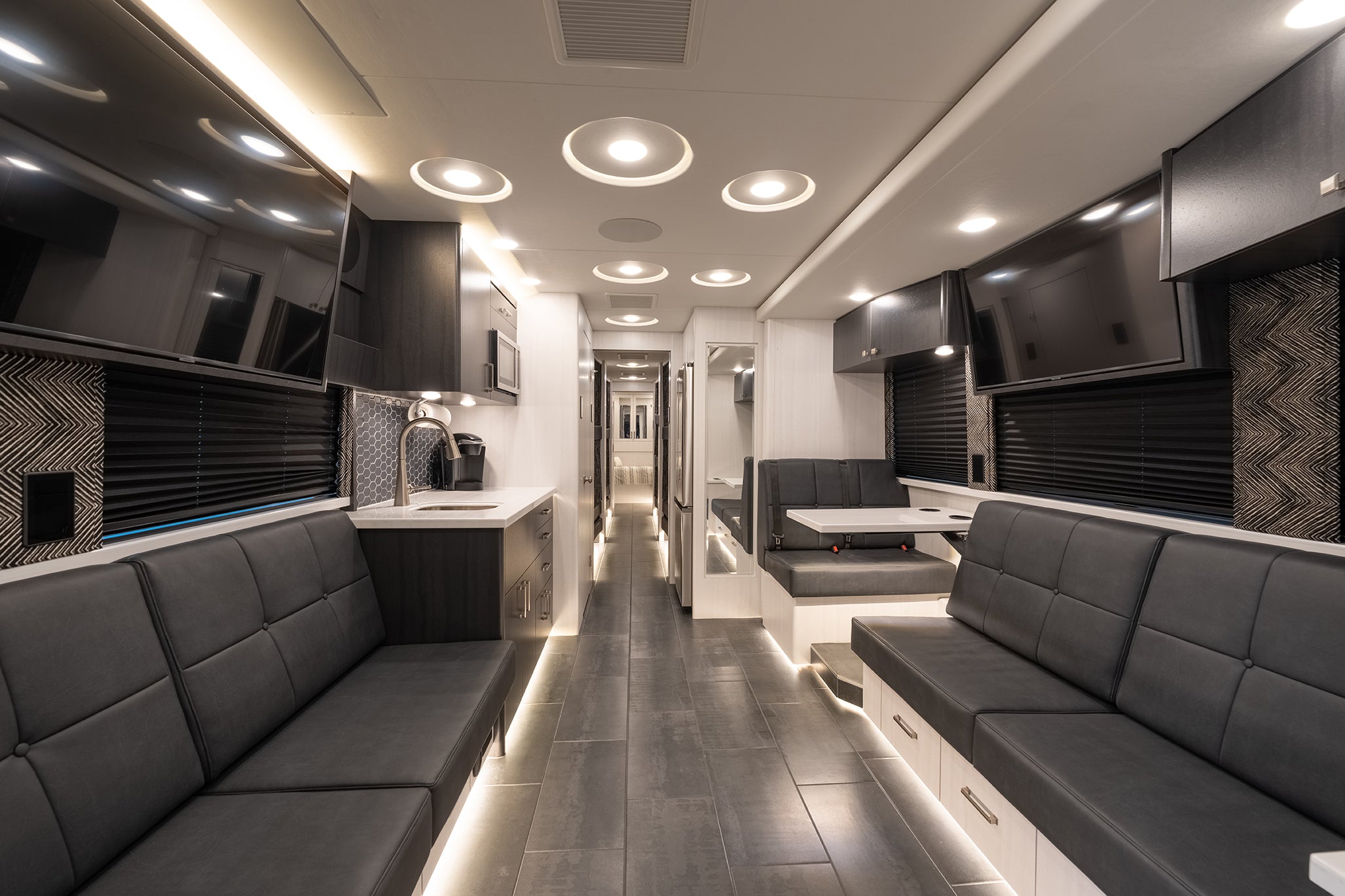 Modern interior of a motorhome with gray couches, kitchen area, and entertainment units.