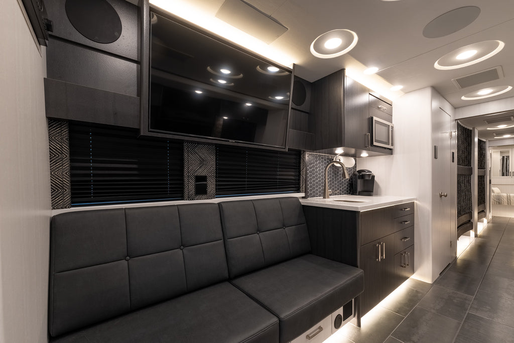 Modern kitchenette with gray couch, TV, and kitchen appliances in a compact living space.