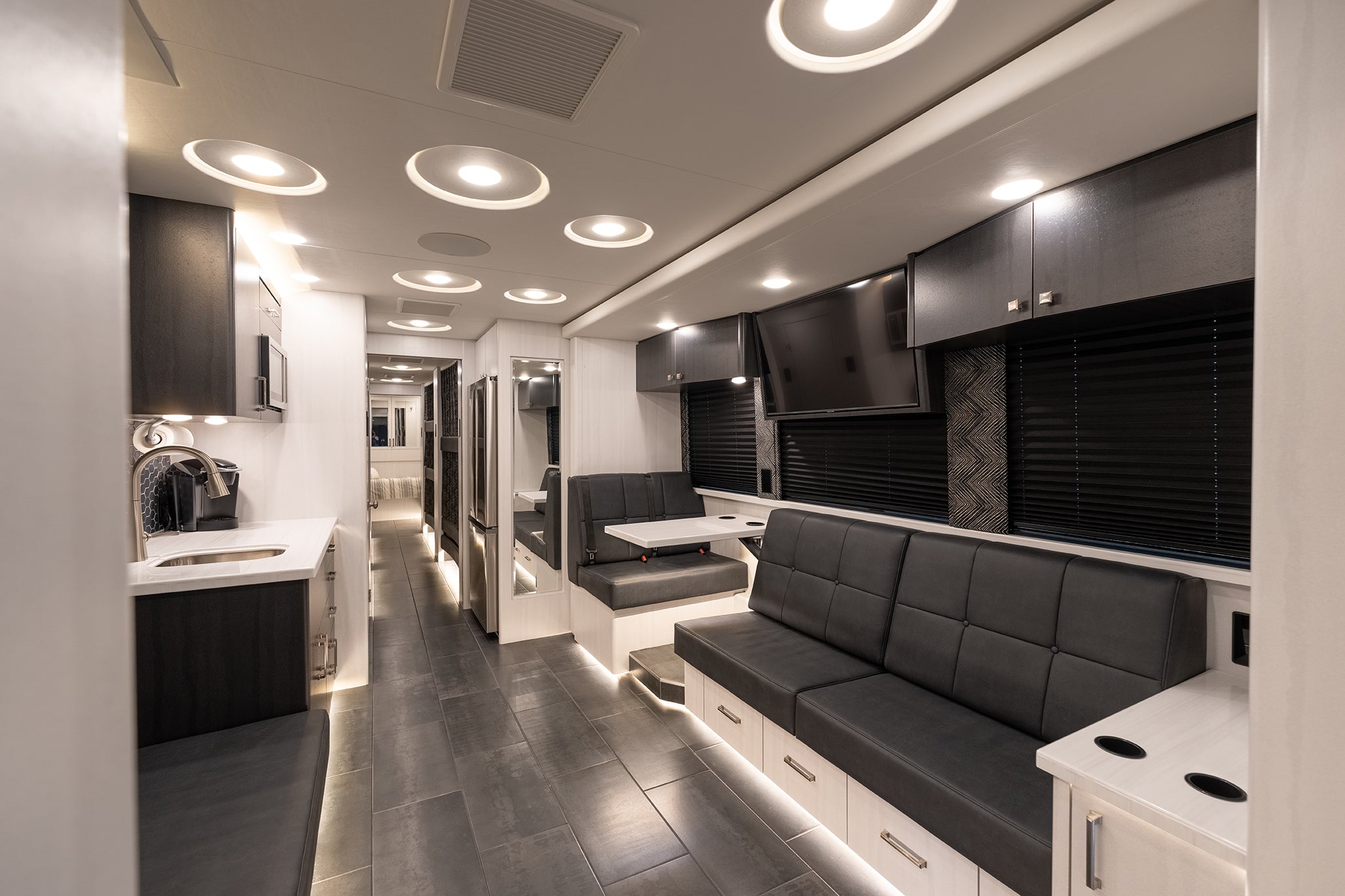 Modern interior of a motorhome with gray couch, kitchen area, and entertainment system.