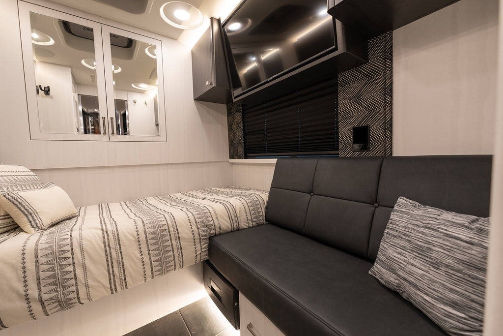 Interior of a vehicle with a bed and black leather bench.