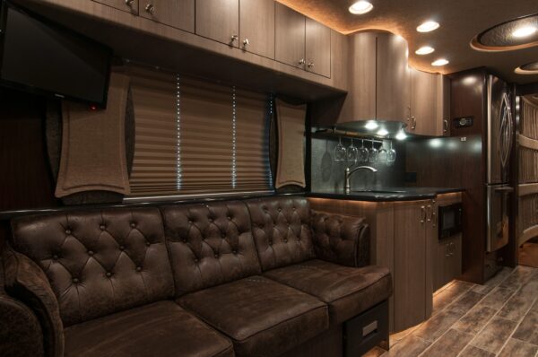 Luxury interior of a recreational vehicle with brown leather couch, kitchen area, and entertainment system.