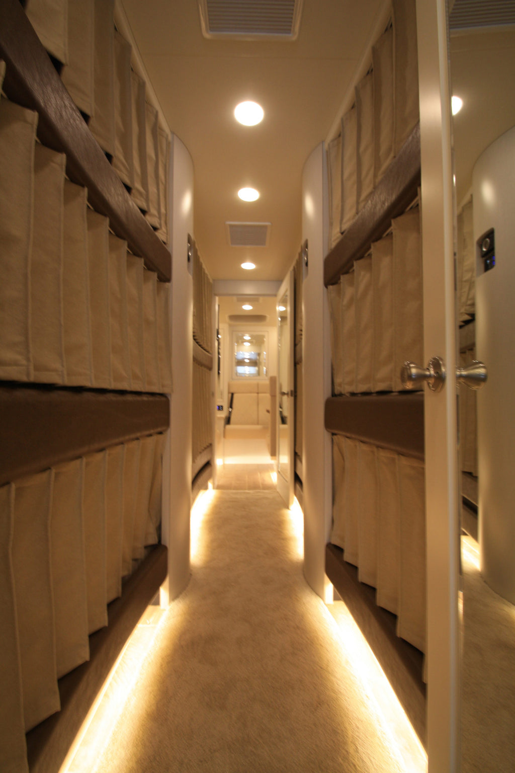 Long narrow room with bunk beds on either side and a lighted floor.