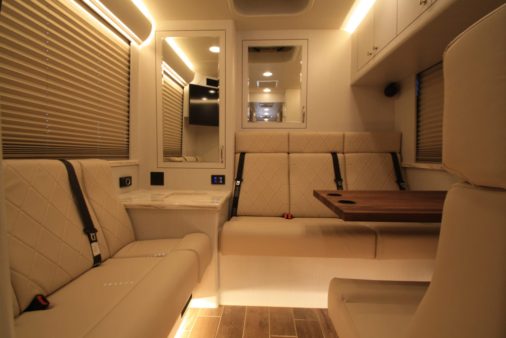 Interior of a modern vehicle with beige seats, wooden table, and reflective surfaces.