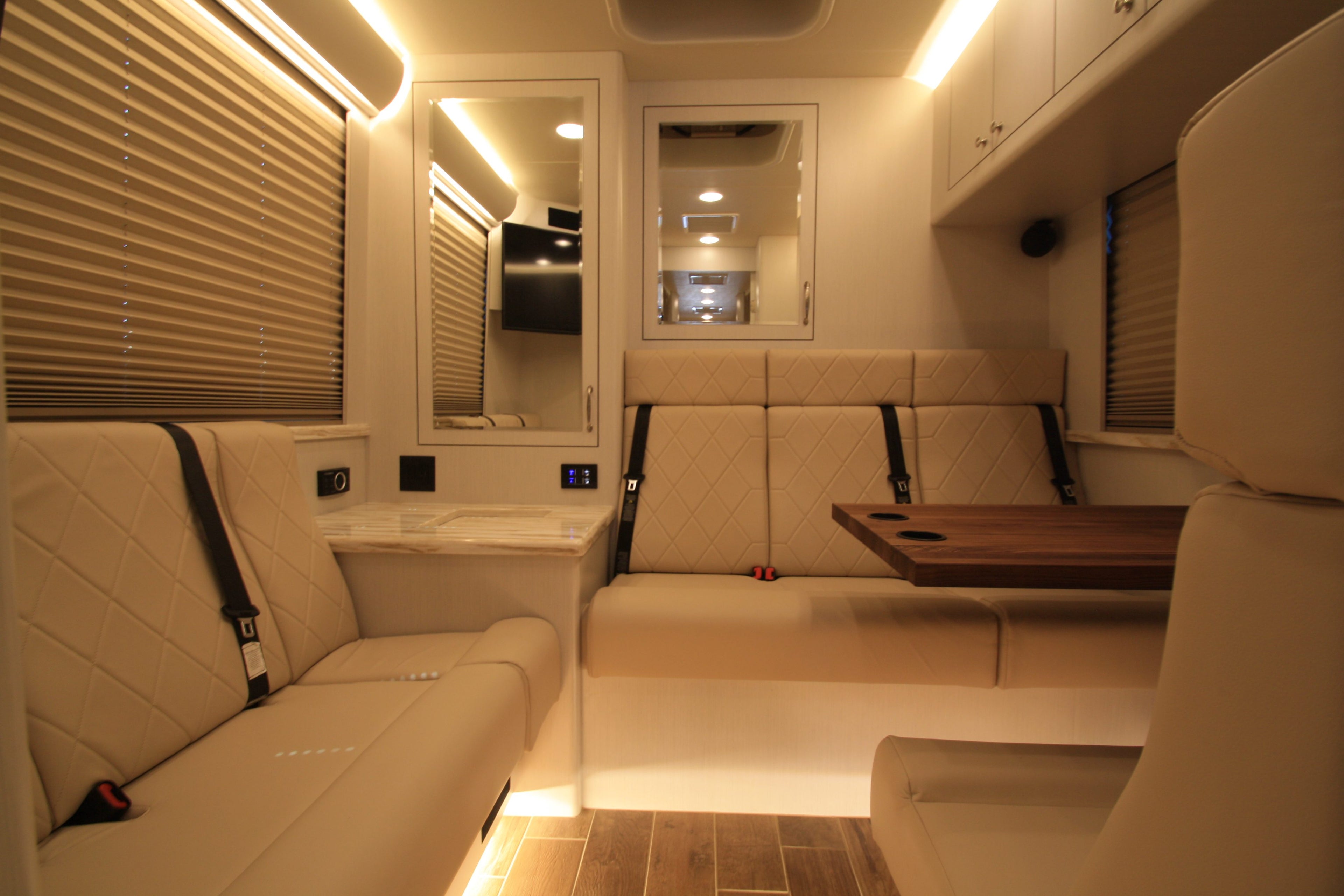 Interior of a modern vehicle with beige seats, wooden table, and reflective surfaces.