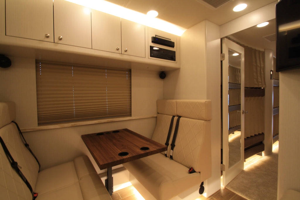 Interior of a compact vehicle with a white couch, wooden table, and cabinets.