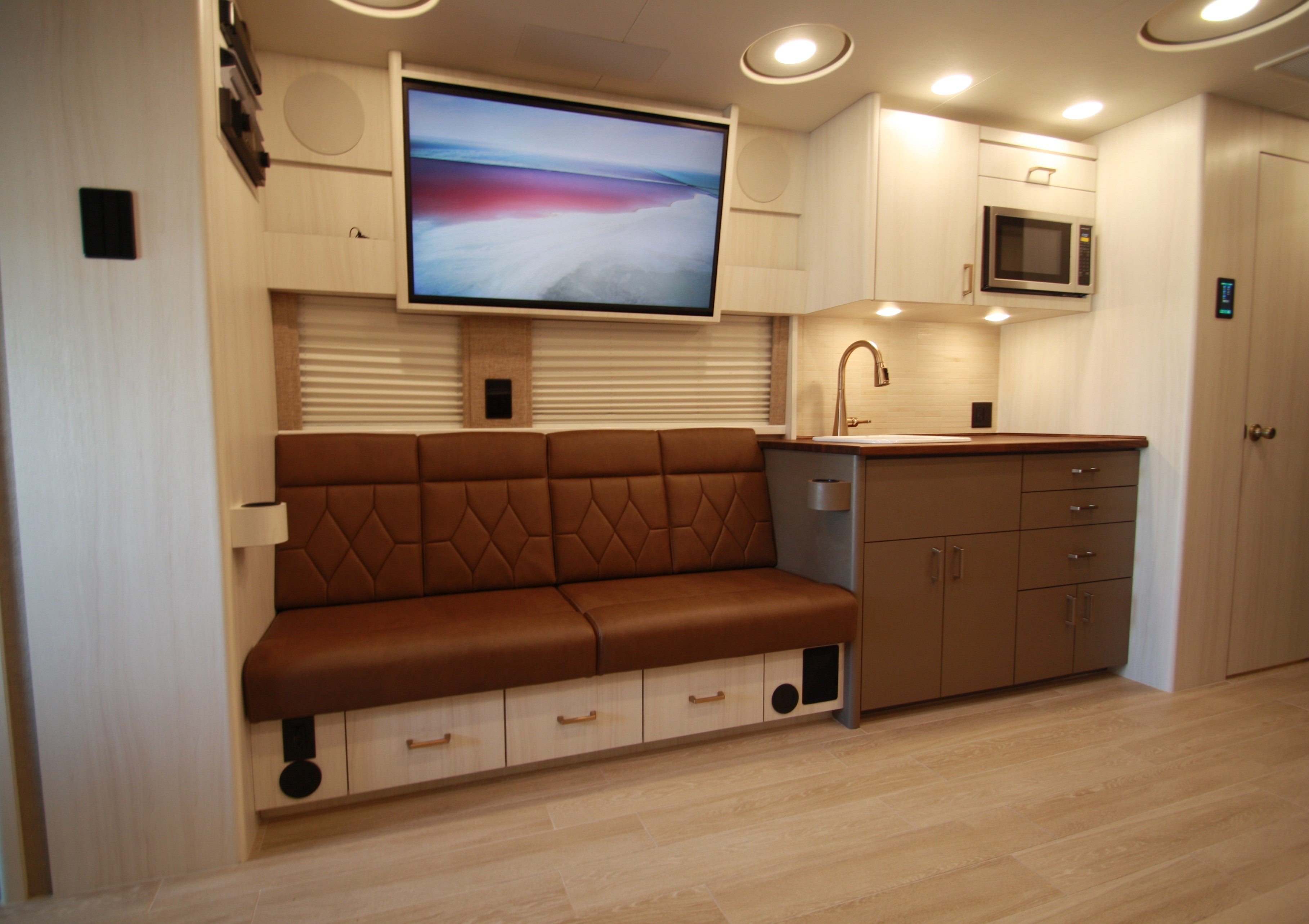 Modern kitchen and living area with brown bench, TV, and cabinets.
